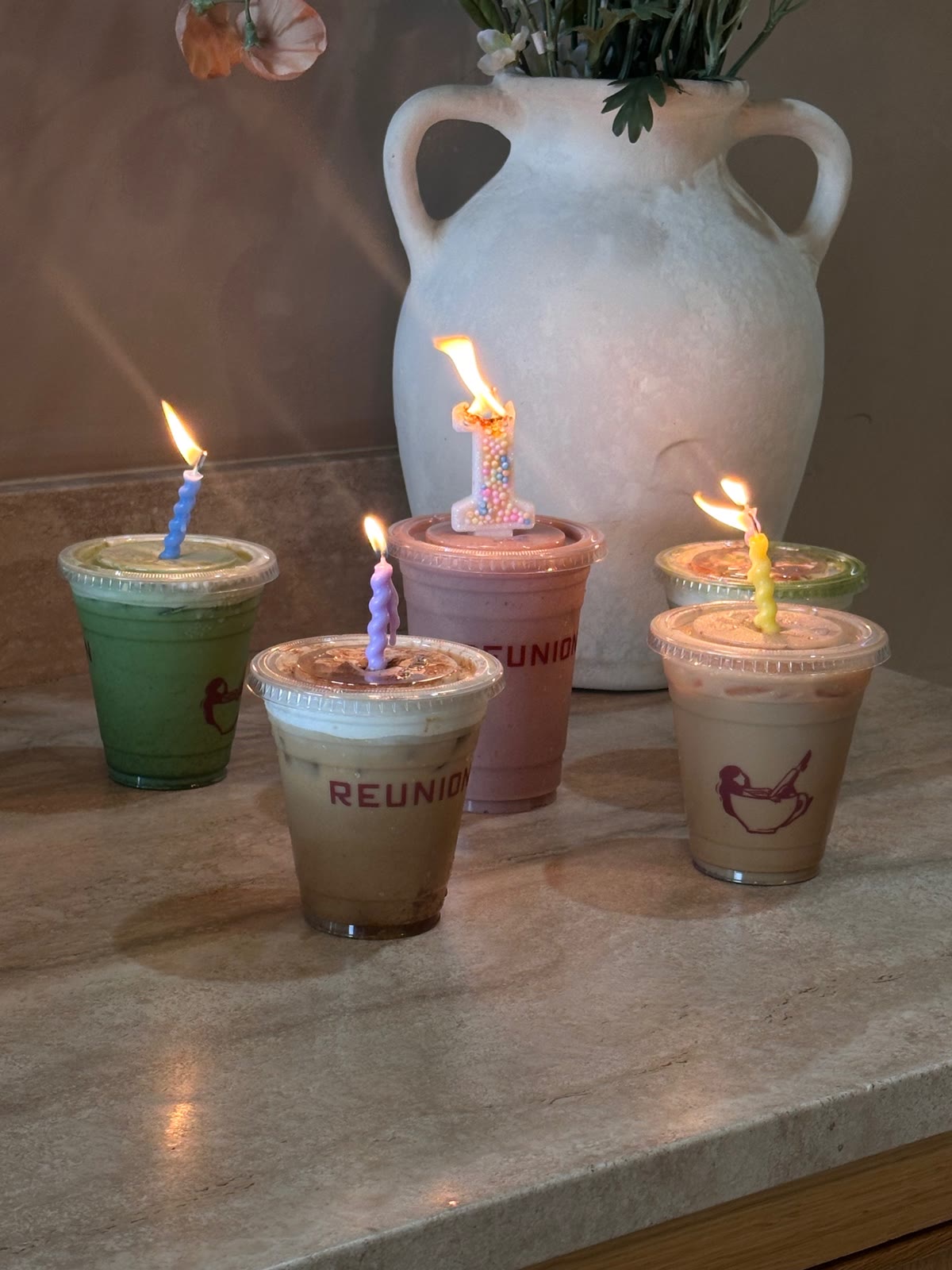 Five Reunion drinks with lit birthday candles, a number one candle in the center